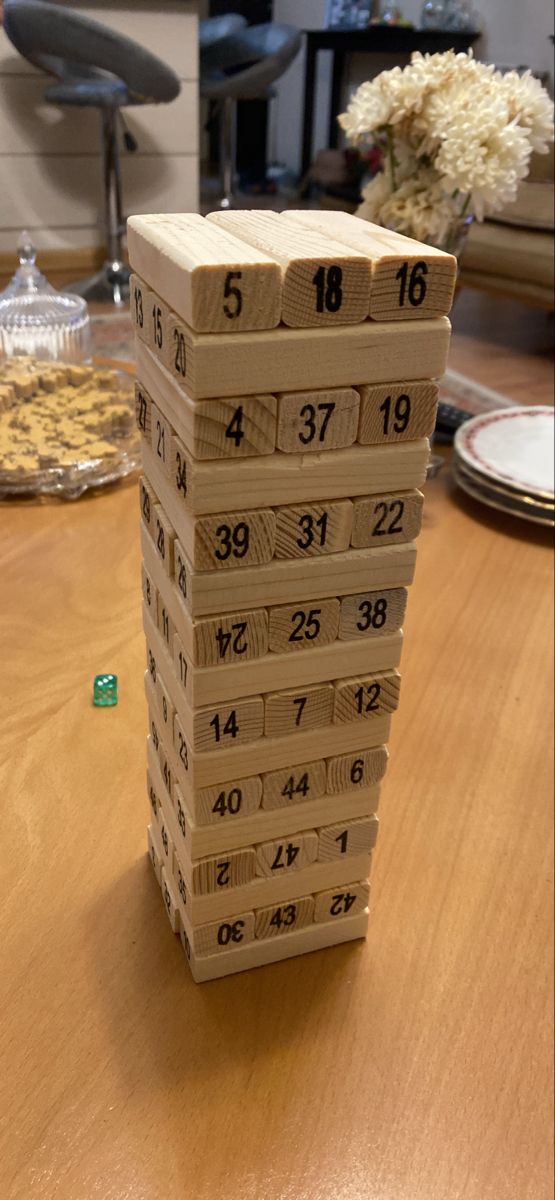 A lifestyle image of a child aged 4–6 seated at a table, fingers gently gripping a numbered block and sliding it from the tower with focused concentration. Natural indoor light, warm background. Communicates the fine motor skill development, concentration, and screen-free learning angle to parents browsing the listing.